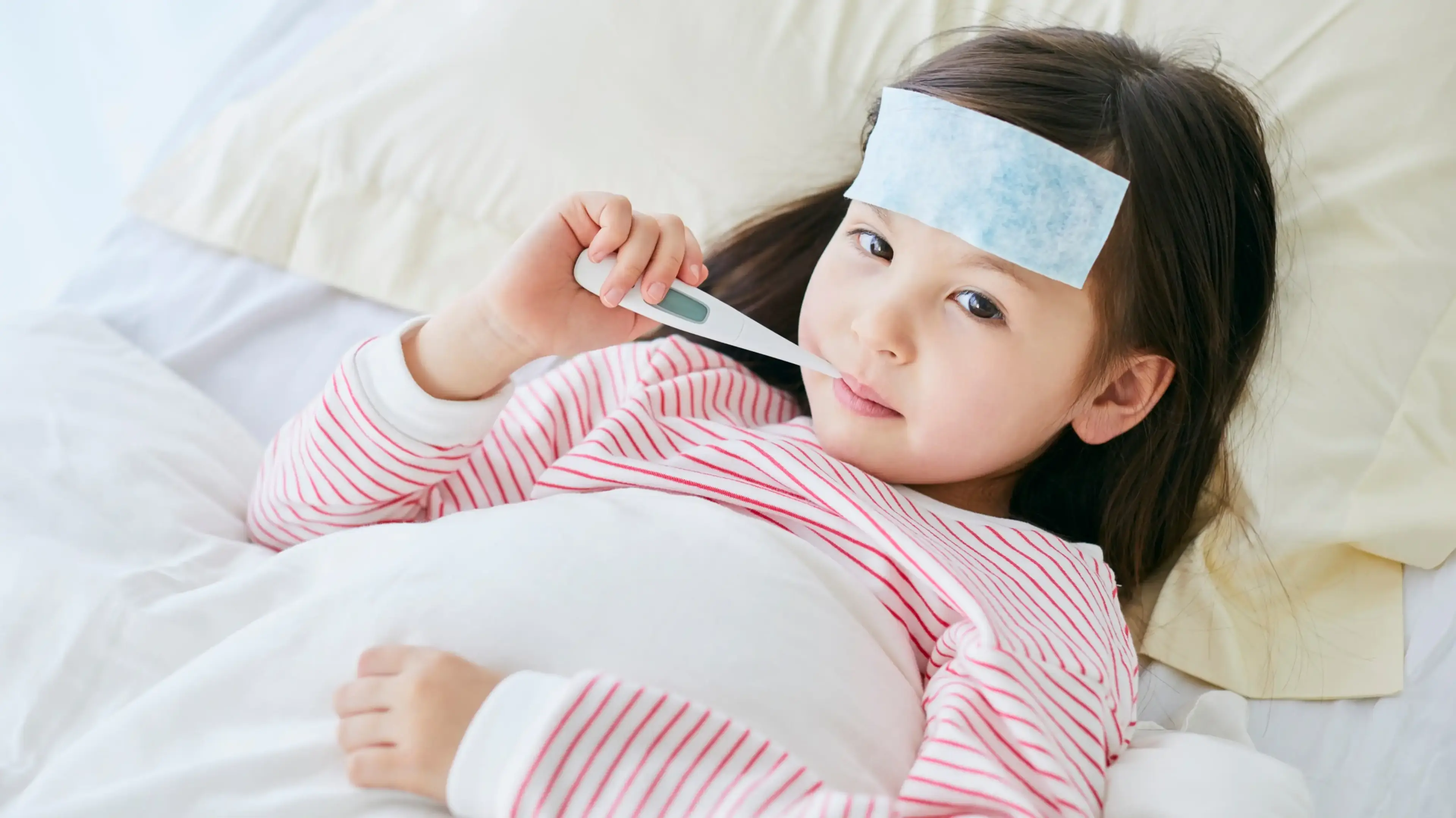 Sick child resting in bed with a thermometer